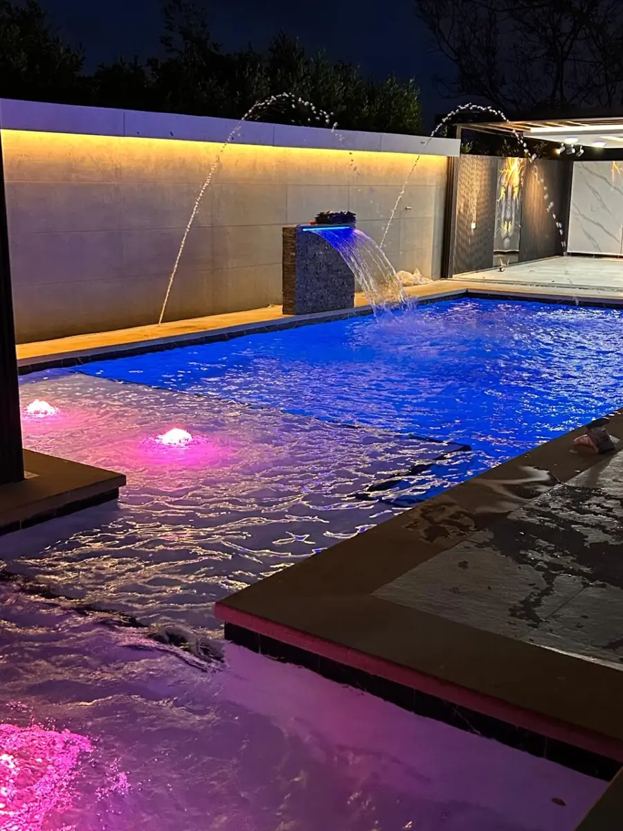 Piscina de noche con cascada, chorros de agua e iluminación LED azul y rosada